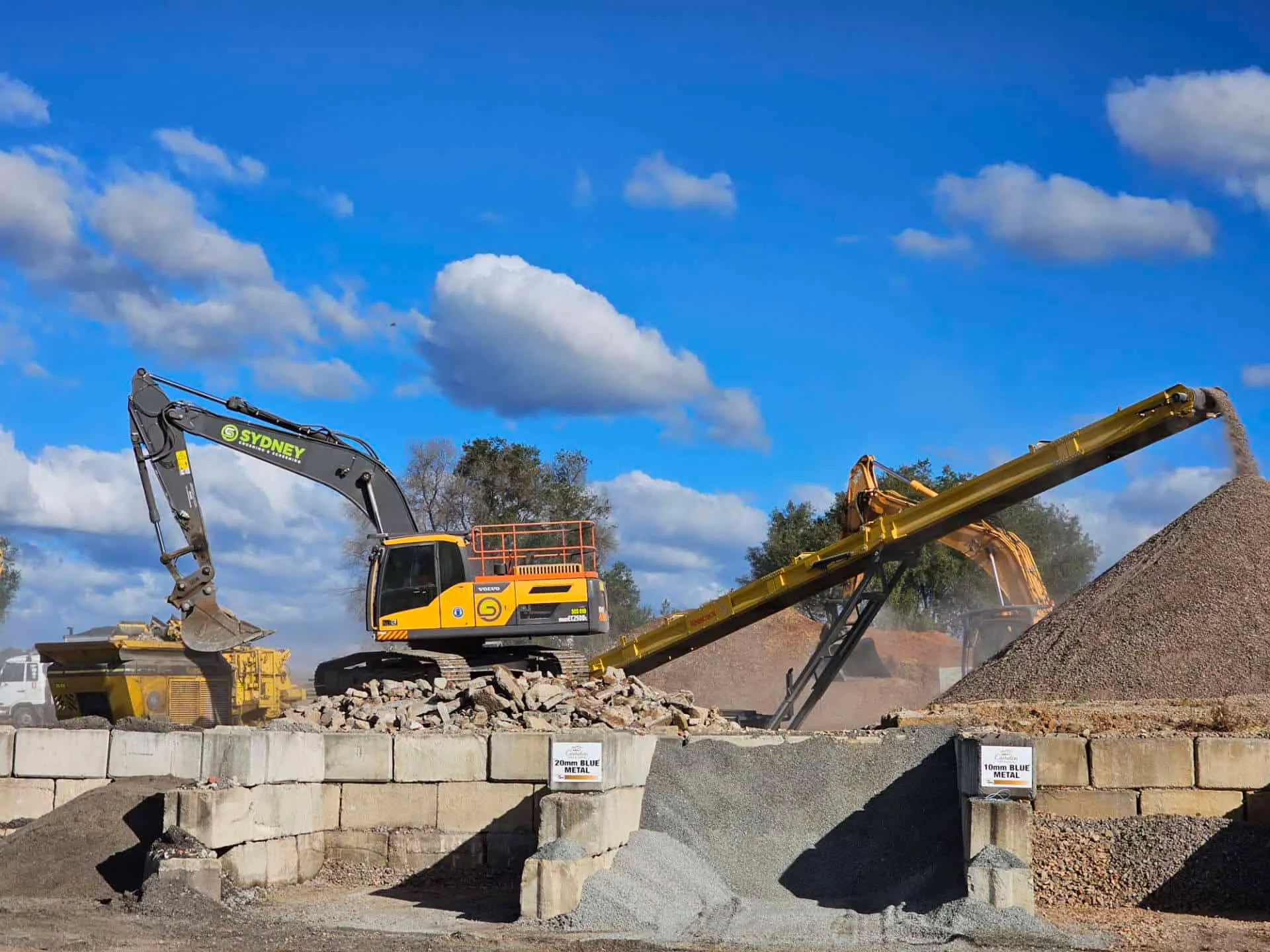 Excavator and conveyor working beside stockpile bays