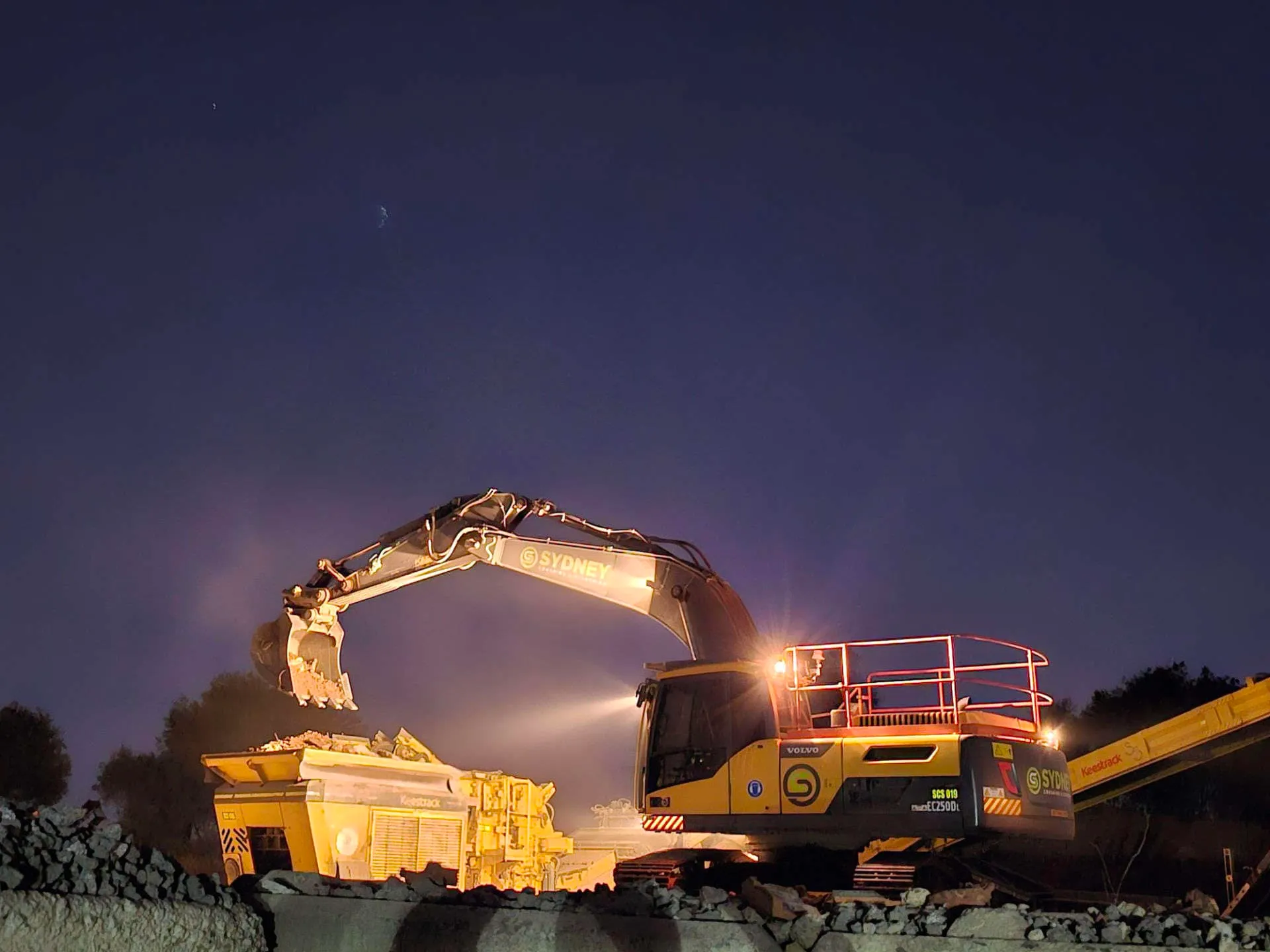 Excavator loading a crusher at dusk