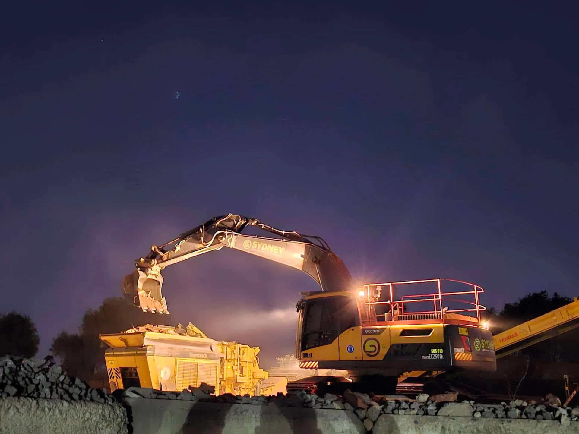 Excavator loading a crusher on a Sydney work site at dusk