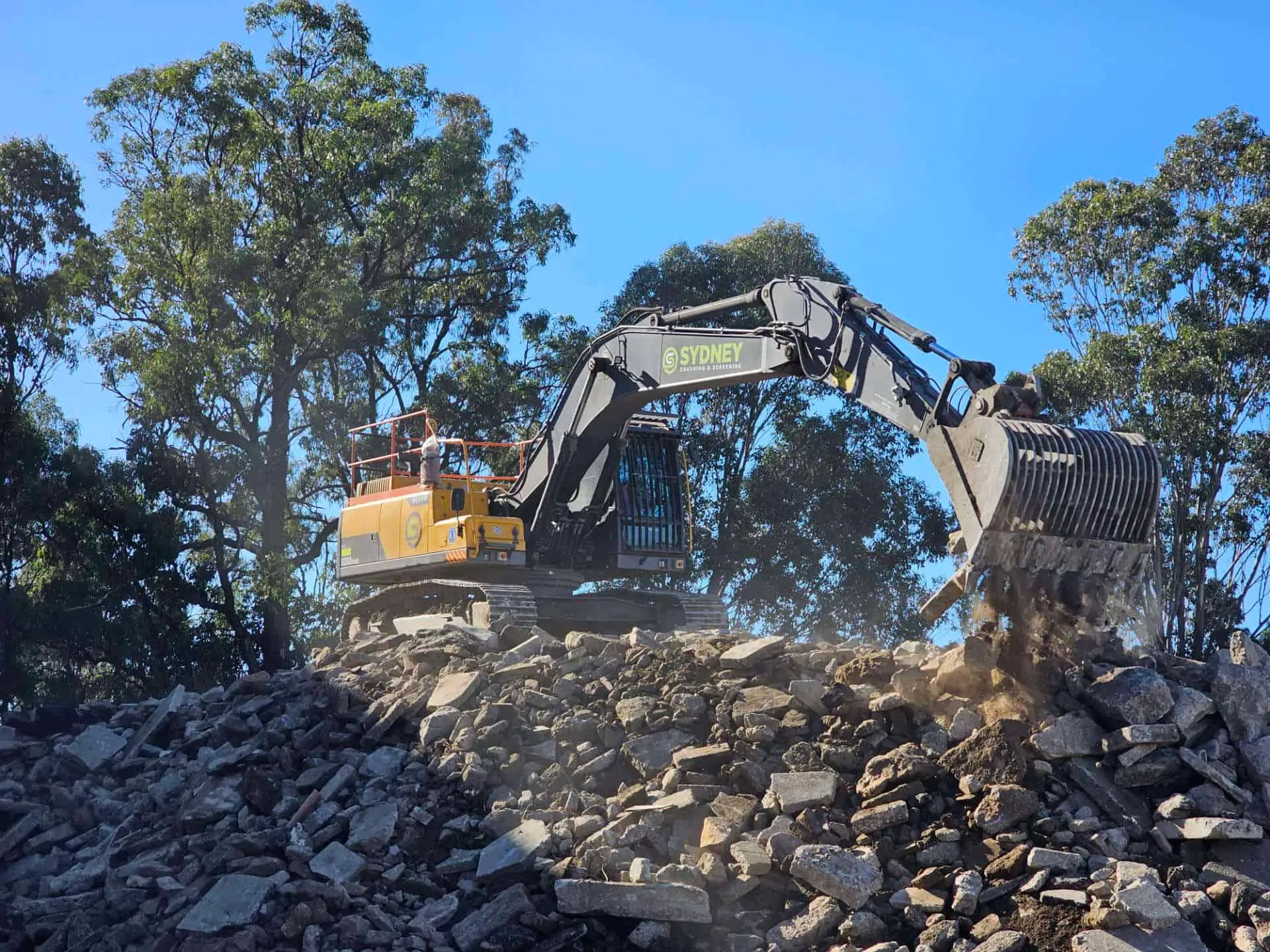 Excavator working a stockpile of broken concrete under a clear sky
